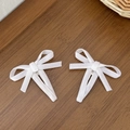 Macro detail of white velvet bow hair clips with silver metal grip on wood surface - White