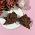 Detail einer braunen Satin-Haarspange mit einem Vintage-Uhranhänger und römischen Ziffern - Braun