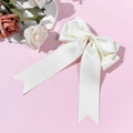 Close-up of elegant white satin ribbon hair clip with long streamers on pink background - Beige