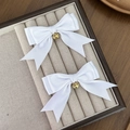 Detailopname van witte satijnen haarstrikken met gouden bellen op een beige fluwelen kussen - Wit