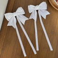 Close-up of white satin bow hair clips with long ribbons on a dark wood texture - White