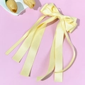 Detailed view of pale yellow satin bow hair clip with elegant long ribbons on pink background - Yellow
