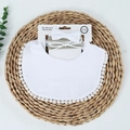 Close-up of white cotton muslin bib with pom-pom trim and matching headbands on straw mat - White