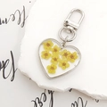 Detail of heart resin keychain with yellow dried flowers on white textured stone - Yellow