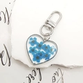 Macro view of a heart-shaped keychain with real blue dried flowers in transparent resin - Blue
