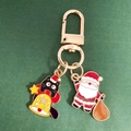 Close-up of enamel Christmas keychains with black cat and Santa Claus charms on green card - Bell Black Cat and Santa Claus