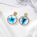 Detailed macro view of golden resin earrings with blue dried flowers on stone pedestal - Blue Floral Earrings