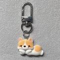 Süßer Cartoon-Corgi-Schlüsselanhänger aus Harz mit silbernem Karabiner auf Lederhintergrund - Gesicht haltender Welpe