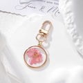 Handmade gold pendant featuring real pink dried flowers inside a clear glass circular frame - Pink Floral Keychain