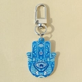 Detail of Hamsa hand keychain with evil eye pattern and blue tribal motifs on beige background - Blue Fish Hamsa