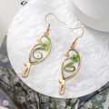Detailed shot of bird-shaped gold earrings with embedded real green dried flowers - Green Flower Bird