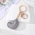 Detail view of a gray leather heart keychain with gold metal ring on a stone stand - Grey Heart
