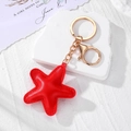 Detail of red star leather keychain with golden clasp on a white stone background - Red