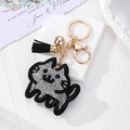 Détail d'un porte-clés chat noir orné de cristaux, gland noir et petite cloche dorée - Chat Noir