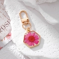 Detailed macro view of a hexagonal gold pendant featuring a real pink daisy in resin - Rose Red Daisy Hexagon