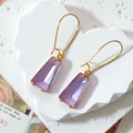 Macro shot of faceted purple glass earrings on a white heart-shaped stone tray - Purple
