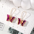 Detailed macro view of golden butterfly hook earrings with purple crystal gradient wings - Purple-Orange