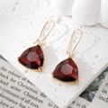 Detail of red triangle crystal earrings with 18K gold hooks on a textured stone base - Brown