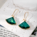 Detailed close-up of dark green fan-shaped crystal earrings with gold trim on stone - Green