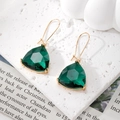 Close-up of dark green geometric crystal earrings with gold hooks on a marble background - Green