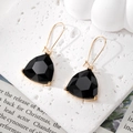 Detail of black geometric crystal earrings with gold trim on white textured background - Black