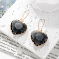 Detalle de pendientes de corazón de cristal negro con borde dorado sobre piedra - Gris