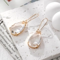 Macro detail of teardrop-shaped crystal earrings with faceted glass and gold plated hooks - Clear