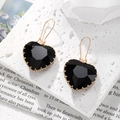 Detalle de pendientes de corazón de cristal negro con gancho dorado sobre piedra rugosa - Negro