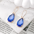 Detail of blue teardrop faceted crystal earrings with gold claw setting on textured surface - Blue