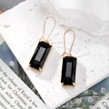 Elegant gold drop earrings with geometric emerald-cut black crystals on white marble - Black