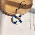 Colgante mini salvavidas de verano con cordón negro sobre un libro vintage - Azul