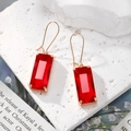 Détails rapprochés de boucles d'oreilles dorées avec cristaux rouges rectangulaires - Rouge