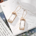 Détail de boucles d'oreilles en cristal avec crochets dorés sur fond blanc texturé - Transparent