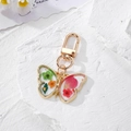 Macro-opname van vlinder sleutelhanger met echte droogbloemen op witte steen - Rode En Groene Bloem Vlinder Stijl