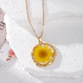 Macro shot of a golden irregular round pendant featuring real dried yellow daisy flowers - Yellow