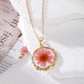 Close-up of clear resin pendant with real pink daisy flower and golden wavy metal frame - Pink