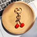 Dettaglio portachiavi a ciliegia con chiusura a cuore dorata su un vassoio di legno - Ciliegia Rossa Senza Foglie