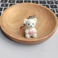 Close-up of a cute white plush bear keychain holding a pink heart in a wooden tray - White Bear