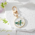 Floral resin keychain with white dried flowers and gold foil in a round metal frame - Green Leaf Floral