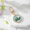 Detail of transparent resin keychain with real fern leaves, blue flowers and gold flakes - Blue Flowers with Green Leaves