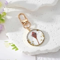 Detail of round resin keychain with real red dried flower bud and gold foil flakes - June Rose Bud