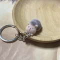 Miniature plush hedgehog keychain with fluffy pink face and grey body on a wooden tray - Open-eyed Lying Hedgehog