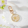Golden keychain featuring a transparent resin pendant with white dried flowers and gold leaf - White Flower