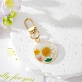 Détail d'un porte-clés rond en résine avec fleurs séchées et crochet en métal doré - Fleur Marguerite Blanche
