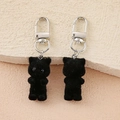 Detail view of two black flocked bear keychains with silver lobster clasps on warm background - Black Flocked Cat
