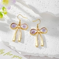 Close-up of golden bow earrings with purple dried flowers and gold foil accents - Purple Rose Green Leaf