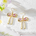 Detail of gold bow earrings featuring preserved pink rose buds in clear resin - Purple Flower