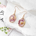 Detailed close-up of handmade resin drop earrings with dried flowers and wire wrap - Purple White Style