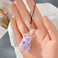 Detail view of purple flocked bear keychain with pink paws and yellow bow on model hand - MR75 Purple Bear