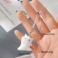 Detail eines weißen beflockten Katzenanhängers mit Band, Verschluss und Maßen - Seitlich sitzende weiße Katze mit Pfote oben (18MR41)